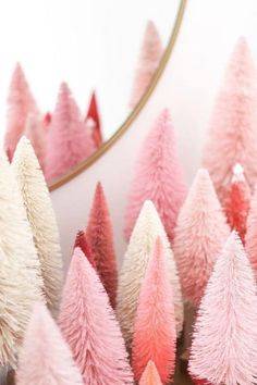 pink and white christmas trees are in front of a mirror with a gold trimming