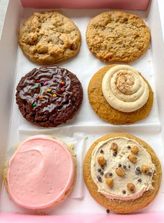 an assortment of cookies and desserts in a pink box with frosting on top