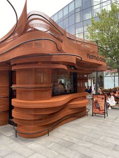 people are sitting at tables in front of a large wooden structure with curved sides and an awning