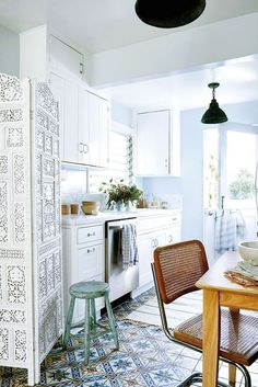 a kitchen with white cabinets and blue tile flooring on the walls, along with a wooden dining table surrounded by wicker chairs