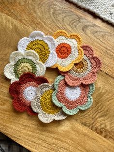 six crocheted flower coasters sitting on top of a wooden table next to a rug