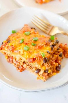 a slice of mexican casserole on a white plate with a fork next to it