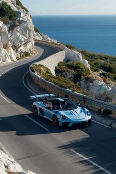 a blue and white sports car driving down a road next to the ocean on a sunny day