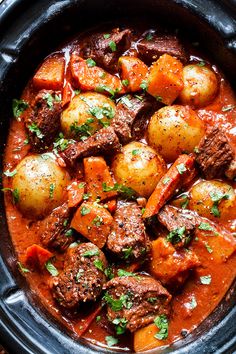 a crock pot filled with beef stew and potatoes, garnished with parsley