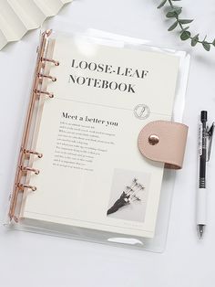 an open notebook sitting on top of a table next to a pen and some flowers