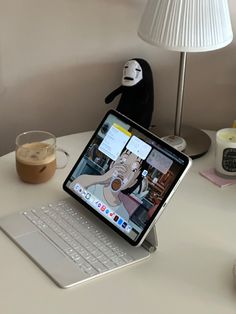 an open laptop computer sitting on top of a white desk next to a cup and lamp