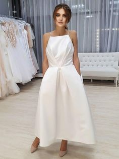 a woman in a white dress standing next to a rack of wedding gowns and dresses