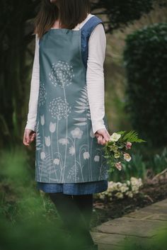 a woman standing in the woods holding a bouquet of flowers and wearing a dress with dandelions on it