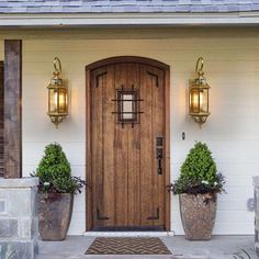 a wooden door with two planters on either side and one light on the wall