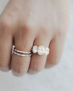 a woman's hand with two rings on it and an engagement ring in the middle