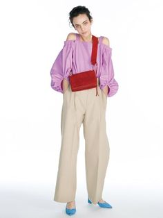 a woman standing in front of a white background wearing a purple top and tan pants