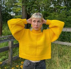 a woman with blonde hair wearing a yellow sweater and jeans stands in front of a fence