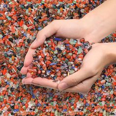 two hands holding small pieces of glass in front of a pile of other colored rocks