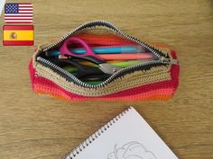 a pencil case filled with markers, scissors and crochet hooks on top of a wooden table