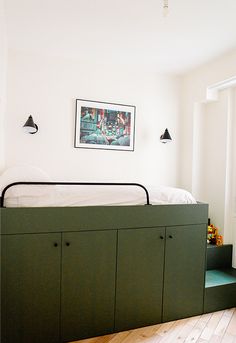 a bed sitting on top of a wooden floor next to a green storage unit in a bedroom