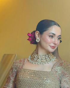 a woman wearing a necklace and earrings with a flower in her hair, standing next to a stair case