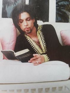 a man reading a book on top of a bed next to a pink pillow and palm trees