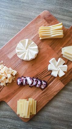 several different types of cheese on a wooden cutting board next to some crackers and grapes