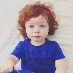 a little boy sitting on top of a bed holding a blue toy bucket and looking at the camera