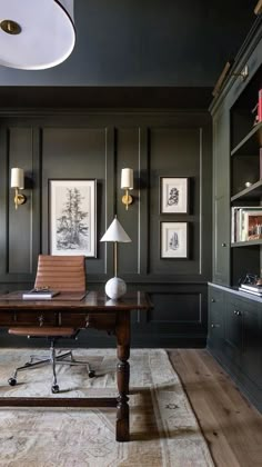 an office with black walls and wooden desk in front of a potted plant on the floor