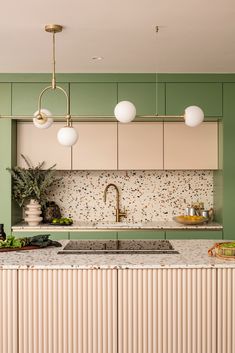 a kitchen with green walls and marble counter tops, brass fixtures and pendant lights hanging from the ceiling