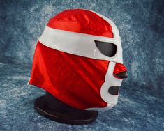 a red and white mask on top of a black head stand against a blue background