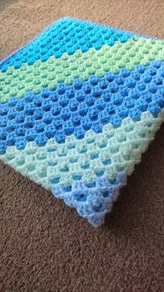 a blue and green crocheted blanket laying on top of a brown carpeted floor