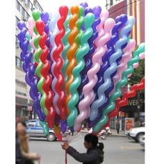 a man is holding up many balloons in the shape of rainbows on a city street