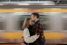 a man and woman standing next to each other in front of a subway train with motion blur