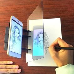 a person is drawing on paper with a pencil and an iphone next to it, while another hand holds a pen