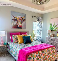 a bed with colorful sheets and pillows in a bedroom next to a painting on the wall