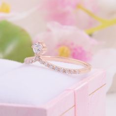 a diamond ring sitting on top of a pink box with flowers in the back ground