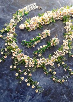 a necklace with white flowers and green leaves on a blue marble surface, in the shape of a heart