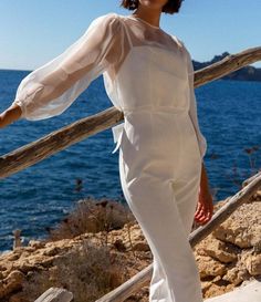 a woman in white is standing on the steps by the water and looking at the camera