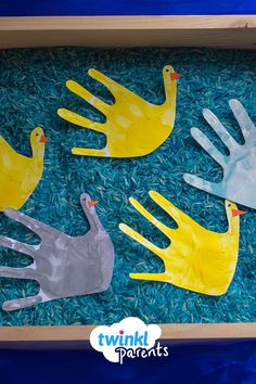 four plastic hand puppets in a box filled with blue and green rice, one is yellow and the other two are gray