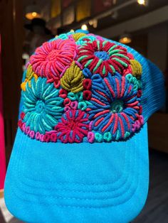 Hand-embroidered in Chiapas, Mexico, these Floral Caps are one-of-a-kind and masterfully crafted pieces. The cap features a vibrant array of flowers, perfect for bringing a pop of color and a touch of style to your look! Perfect for summer, this beautiful cap features a mesh rear for breathability and also has an adjustable head strap! Embroidered Snapback Trucker Hat For Beach, Summer Beach Embroidered Trucker Hat, Embroidered Baseball Cap For Beach, Embroidered Trucker Baseball Cap For Beach, Embroidered Baseball Cap For Beach In Spring, Multicolor Spring Cap, Multicolor Cap For Spring, Adjustable Embroidered Baseball Cap For The Beach, Embroidered Blue Spring Hats