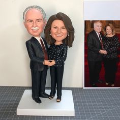 a custom bobble head couple standing next to each other in front of a photo