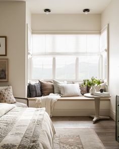 a bed sitting under a window next to a table with a vase on top of it