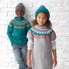 two children standing next to each other wearing sweaters and hats