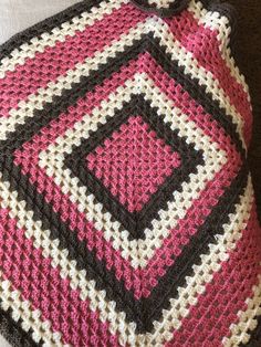 a crocheted pink and black blanket on the floor next to a brown couch