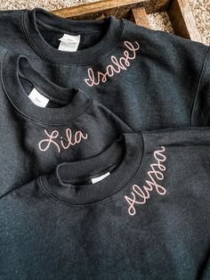 two black sweatshirts with pink lettering on them sitting on the floor next to a wooden box