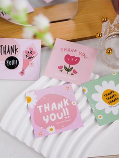 four thank you cards are on a plate with flowers and a vase in the background