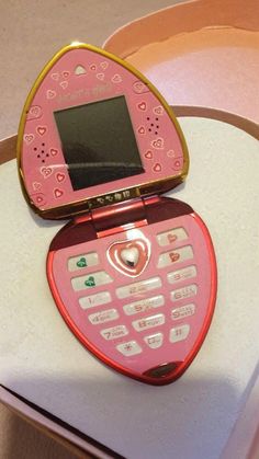 a pink and gold cell phone sitting on top of a white table next to a heart shaped object