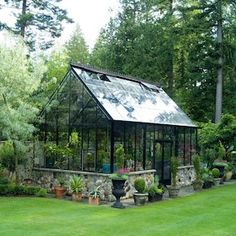 a small glass house in the middle of a green yard with lots of plants and trees