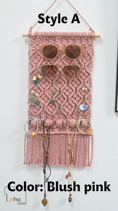 a pink wall hanging with sunglasses and other items attached to the hooks, which are also made out of yarn