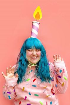 a girl with blue hair wearing a birthday hat and holding her hands in the air