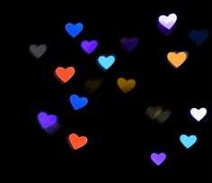 many different colored hearts floating in the air on a black background with blurry lights