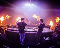 two young men standing next to each other in front of a dj set on fire