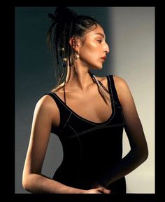 a woman with braids standing in front of a white wall wearing a black dress