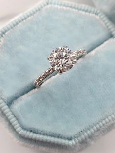 an engagement ring in a blue velvet box with diamonds on the band and side stones